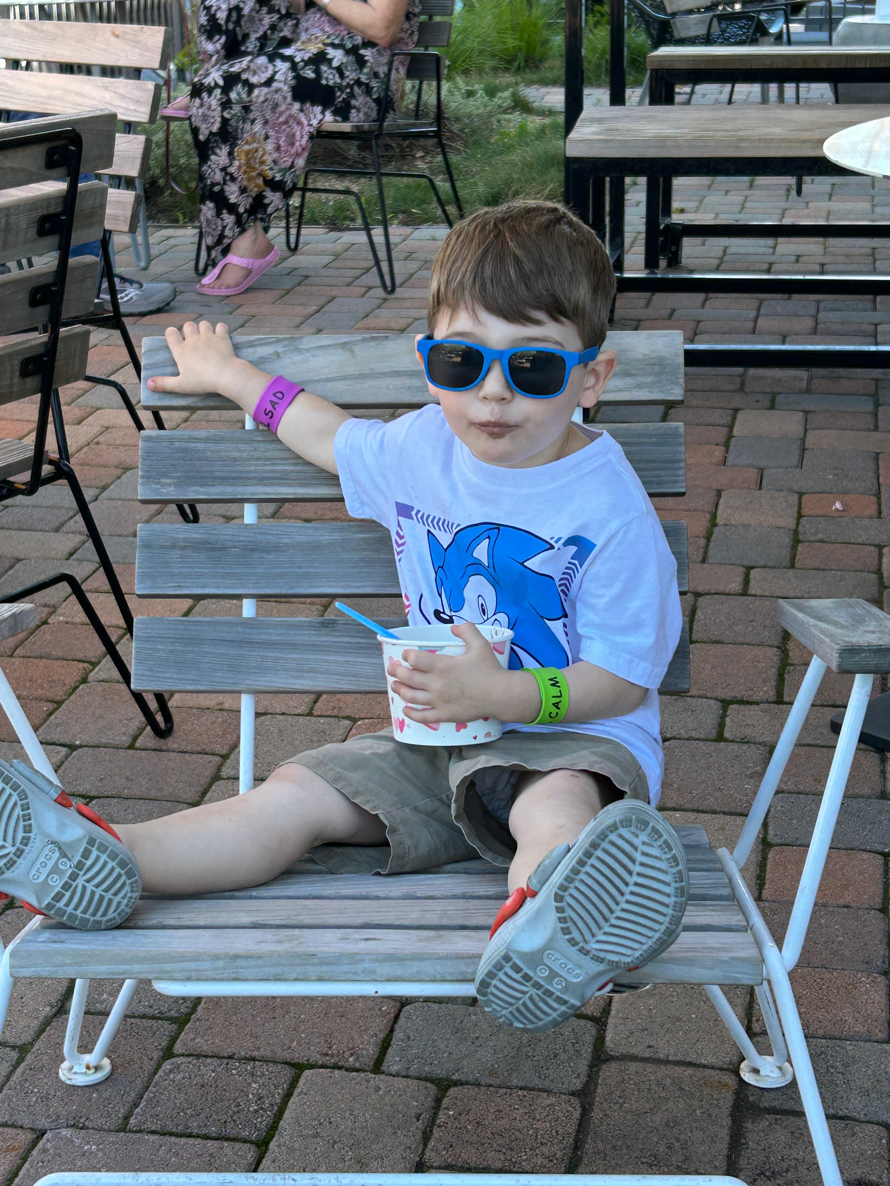 Child sitting on a wooden bench outdoors wearing a Moodles wreistband.