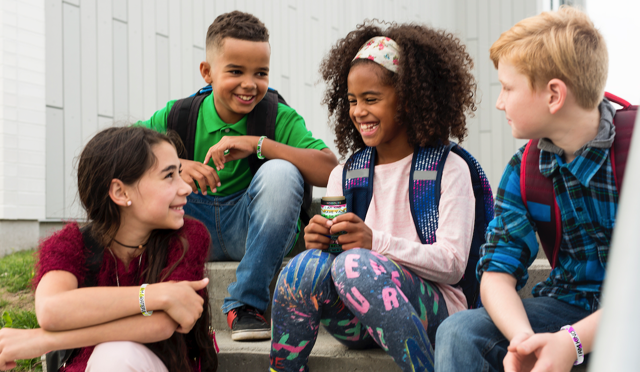 Four children sitting on steps outdoors, smiling and interacting.