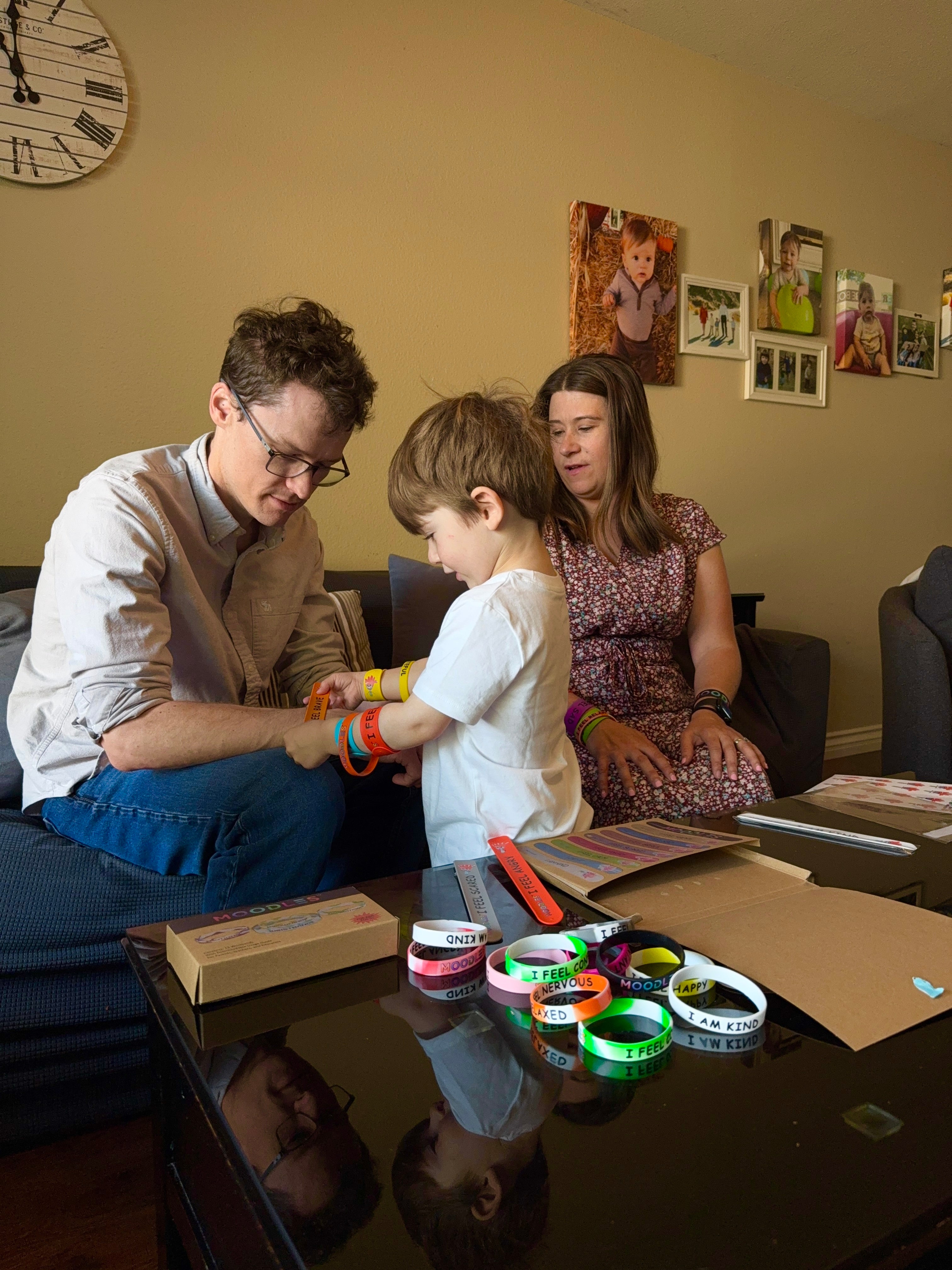 Family in a living room with a child interacting with colorful bracelets on a table.